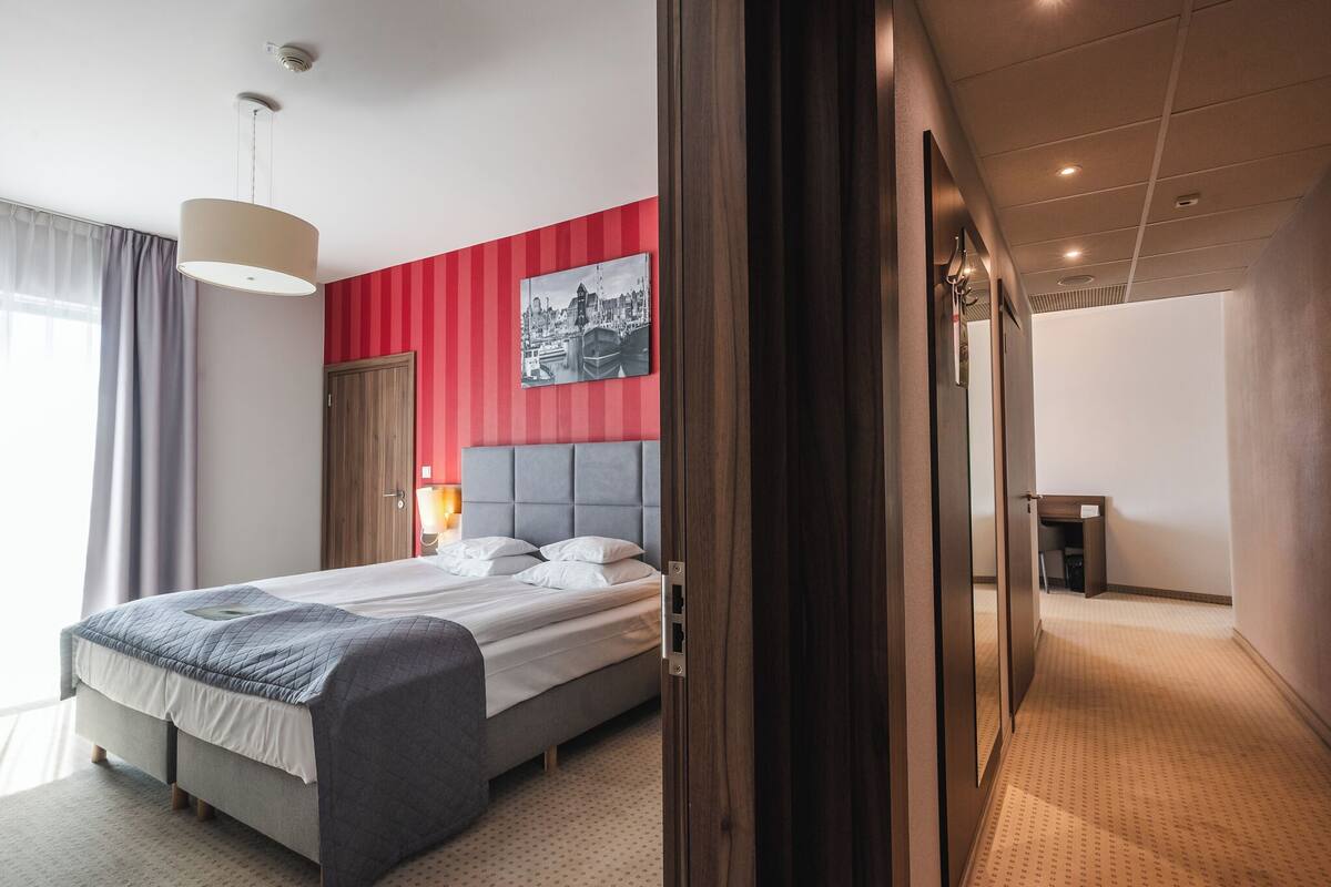 Ein Hotelzimmer mit Bett, einer Wand mit roten Streifen, einem Stadtbildgemälde und einer Holztür.