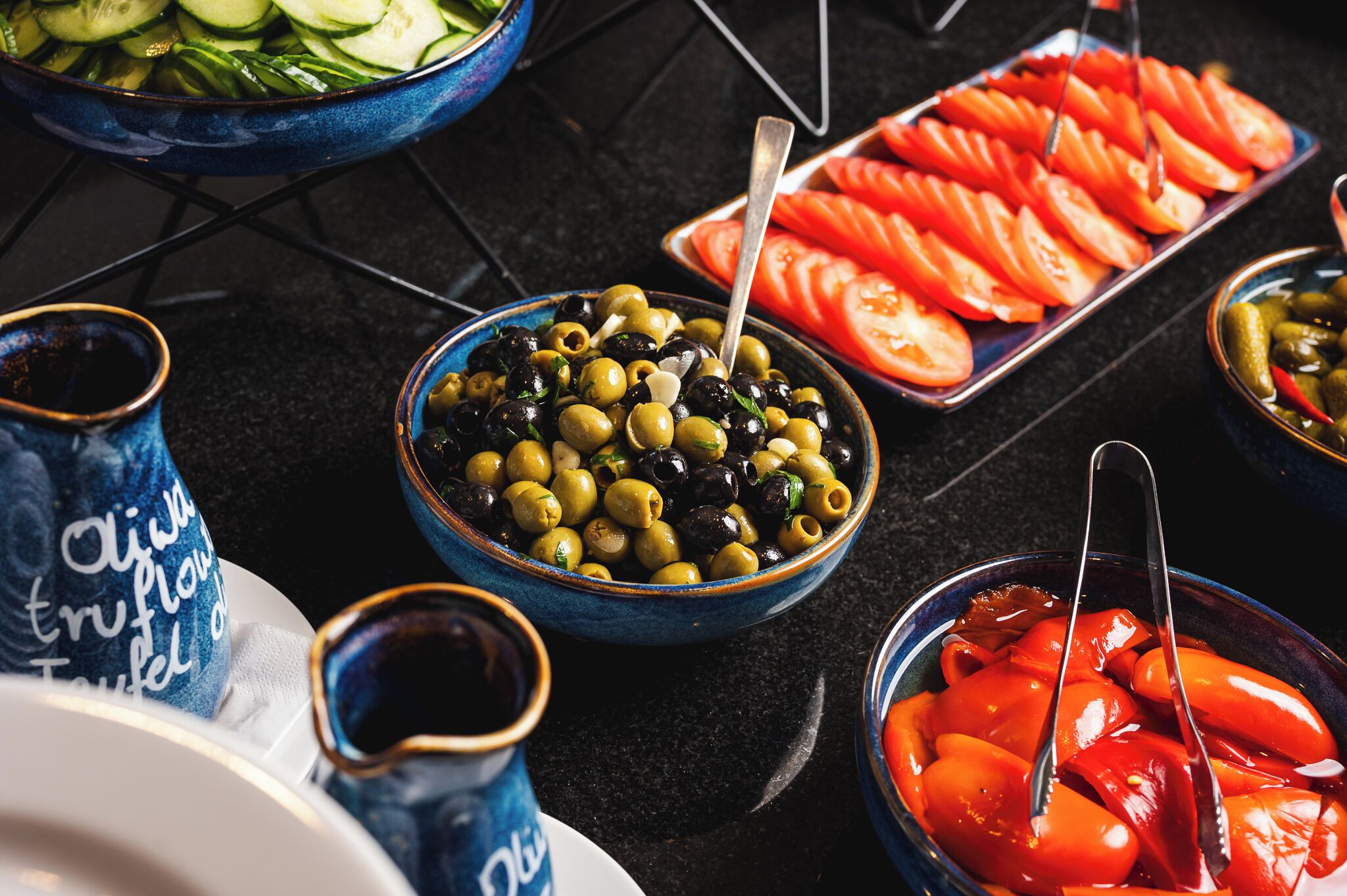 Una mesa de buffet con diversos alimentos, como aceitunas, tomates en rodajas y verduras encurtidas.