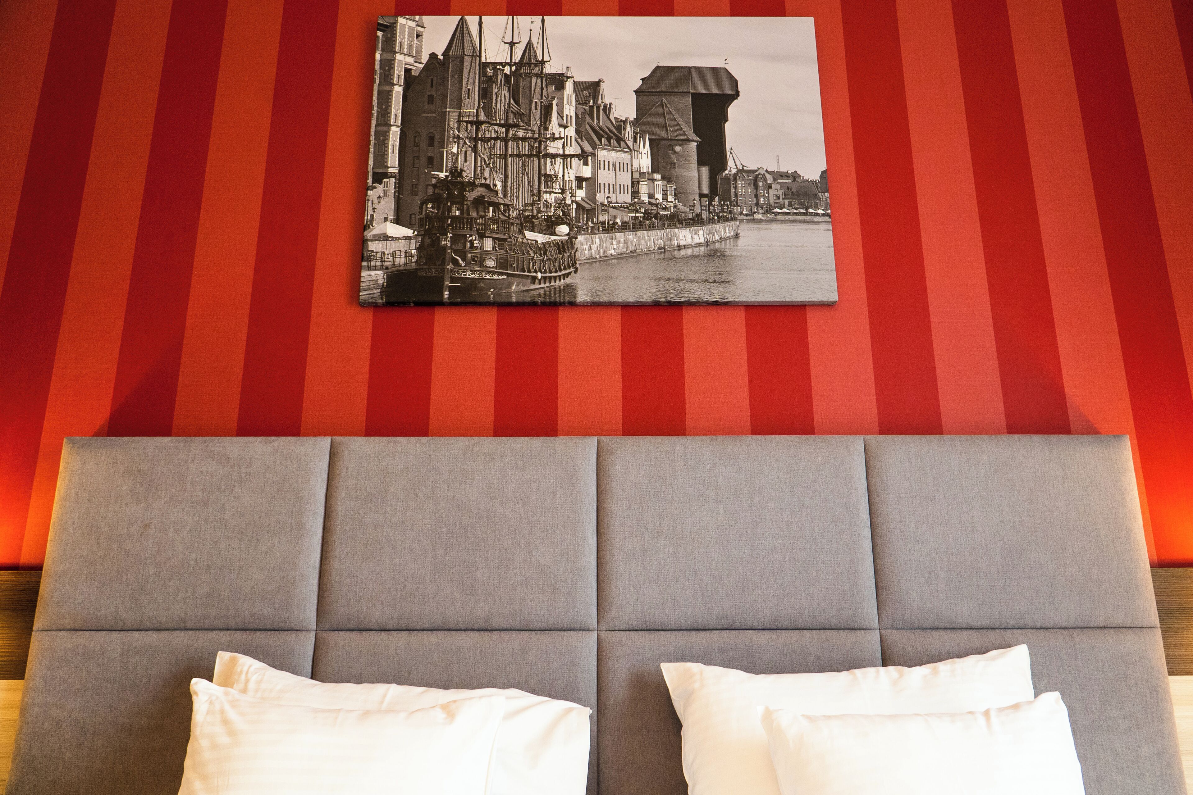 Una habitación de hotel con una cama grande, cabecera y un cuadro de paisaje urbano en la pared.