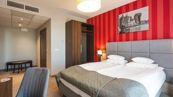 A hotel room with a bed, a bench, a wardrobe, and a red-striped wall with a cityscape painting.