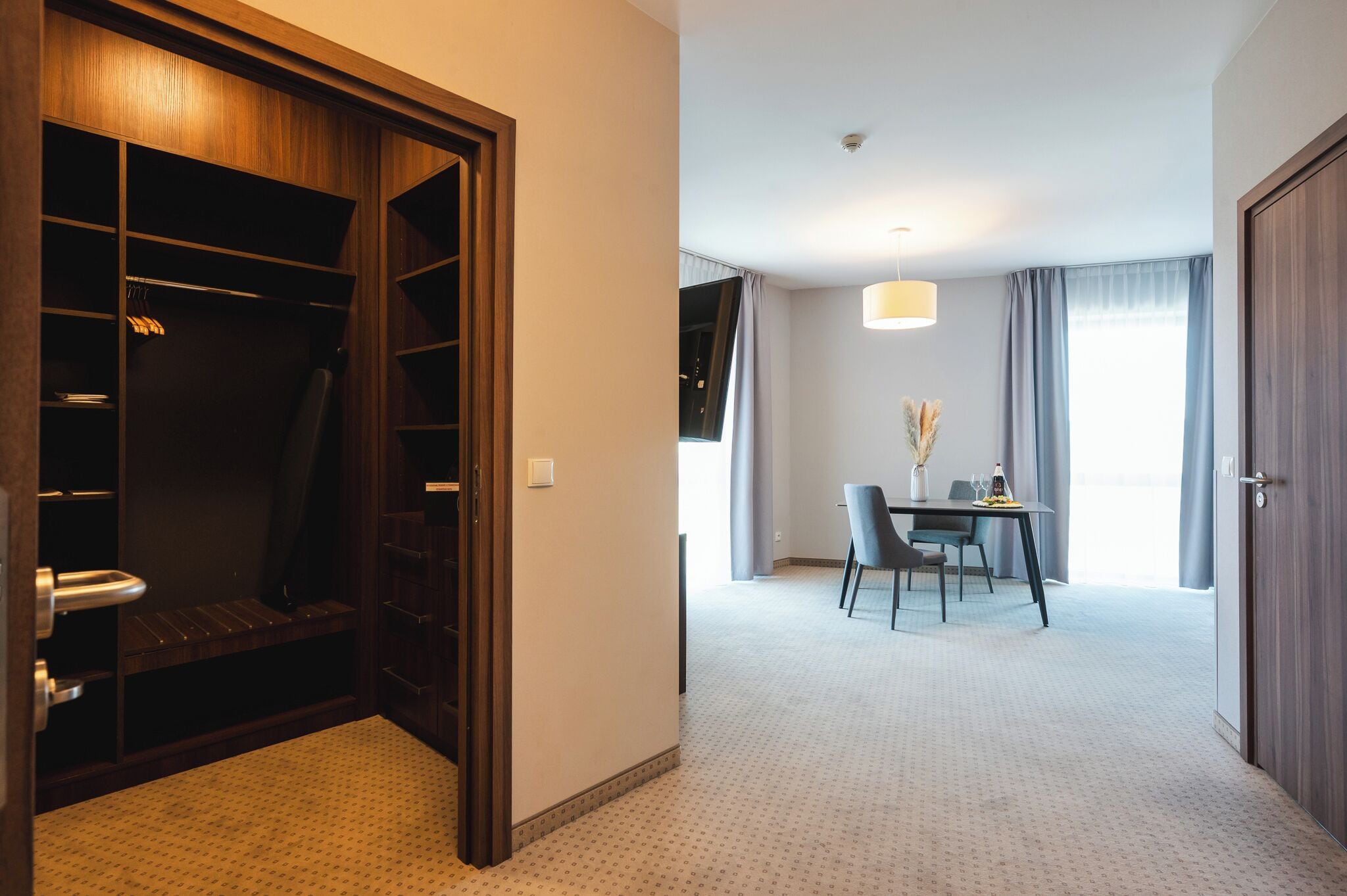A hotel room with a walk-in closet, a dining area with a table and chairs, and a large window with curtains.