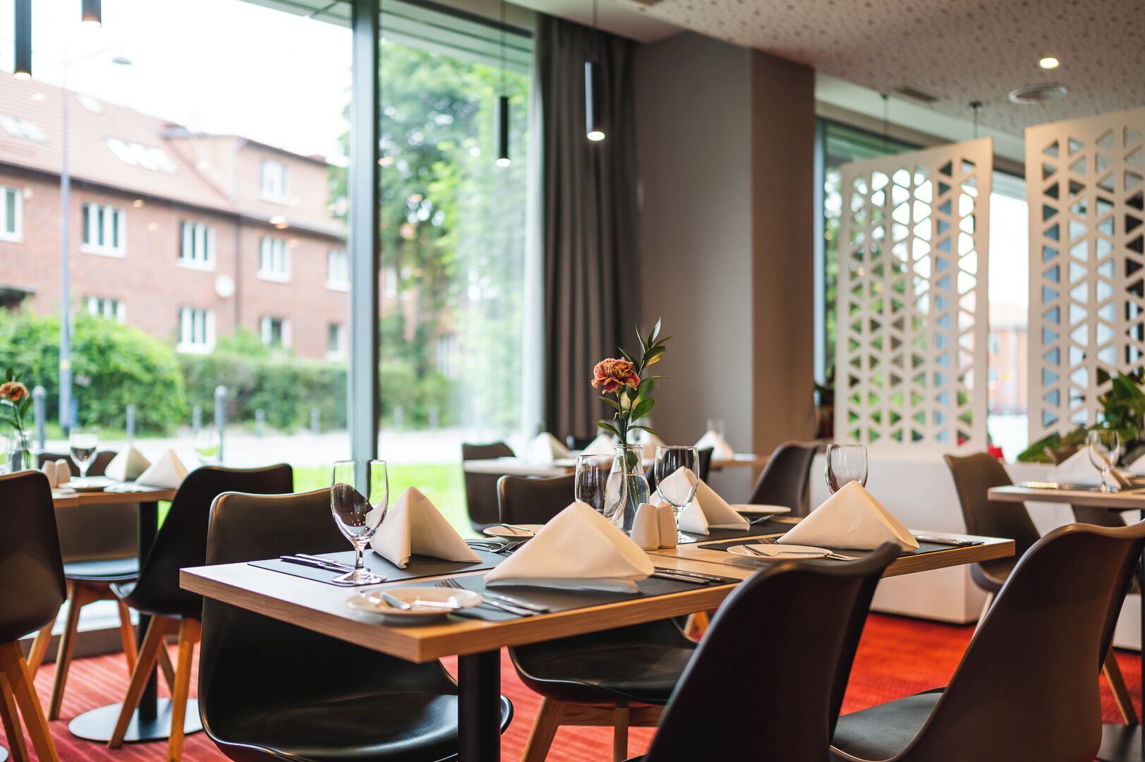 A restaurant with tables set for dining, large windows, and a view of buildings and greenery outside.