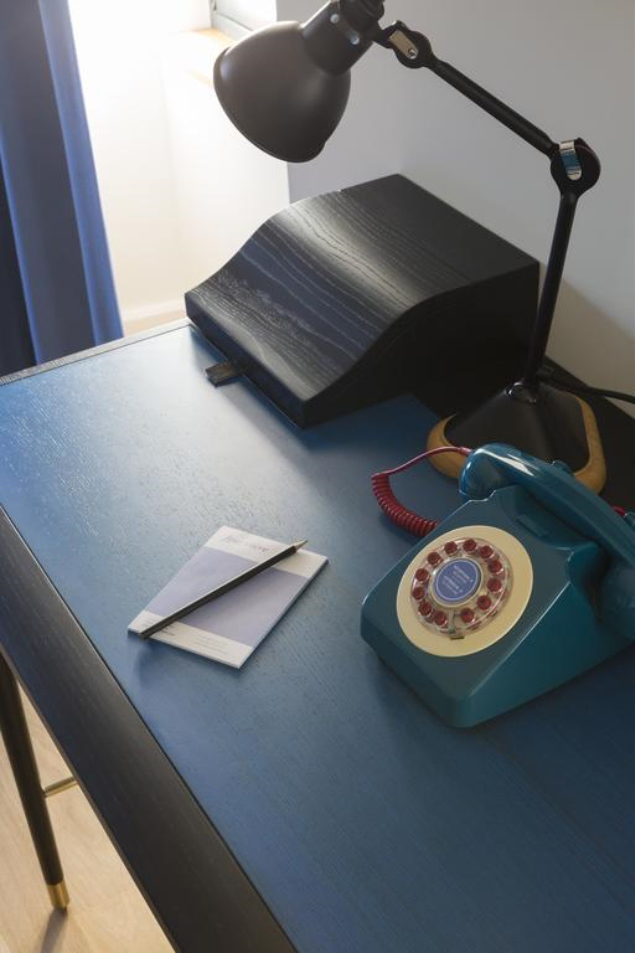A desk with a lamp, a telephone, and a black box.
