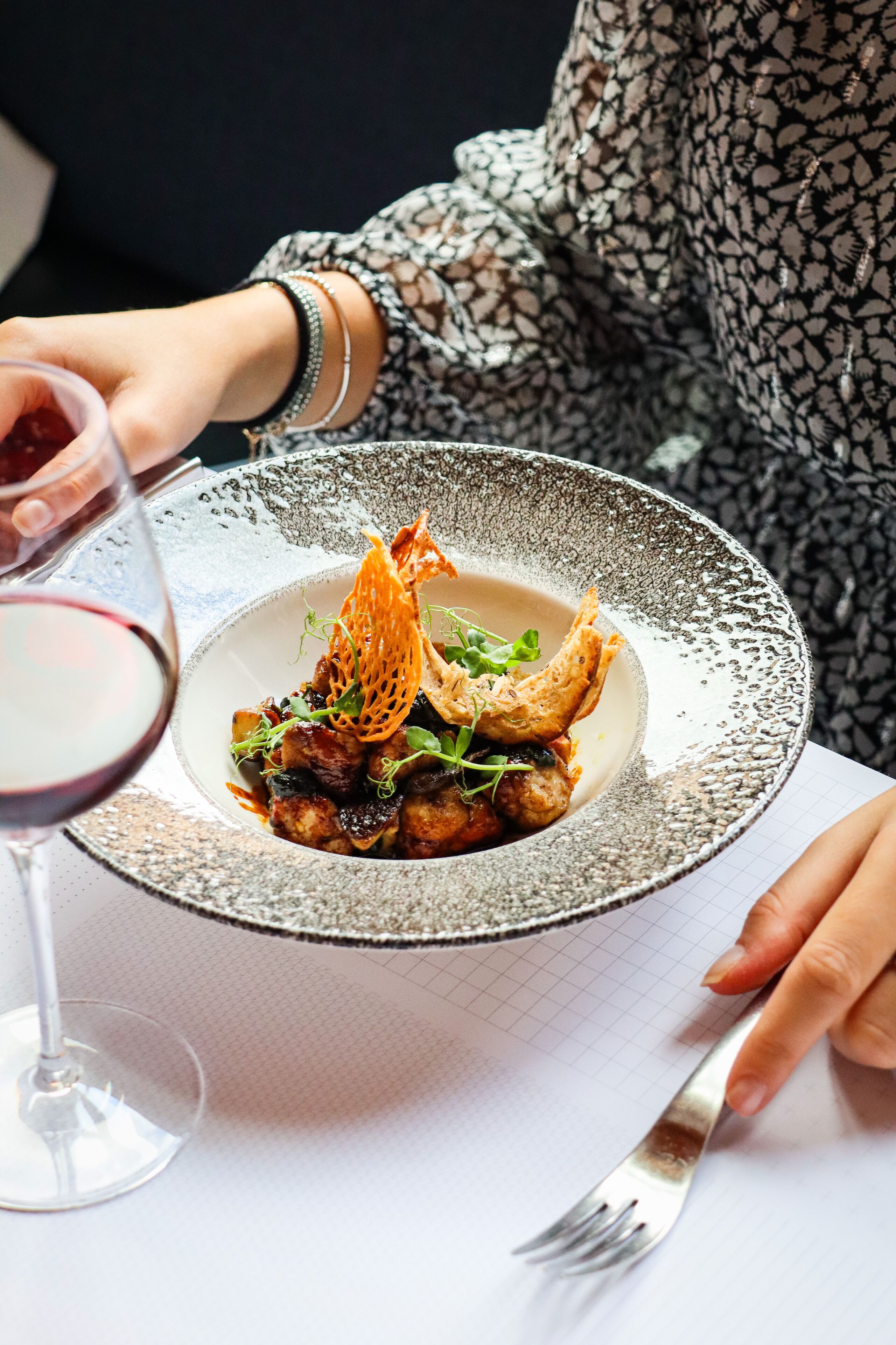 A person dining with a plate of food and a glass of red wine.