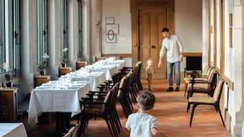 A long corridor with tables set for dining, arched ceilings, and a wooden door at the end.