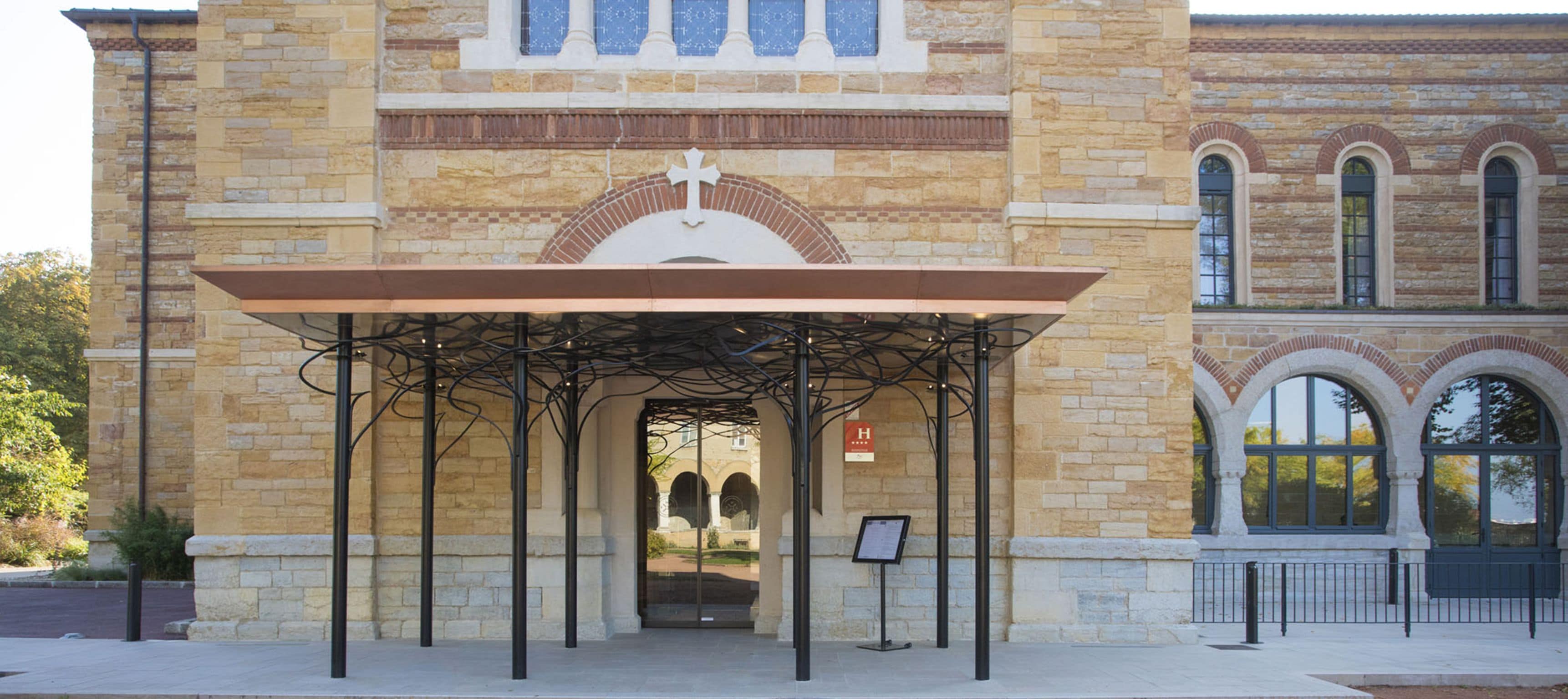 A stone building with a covered entrance and a cross above the door.