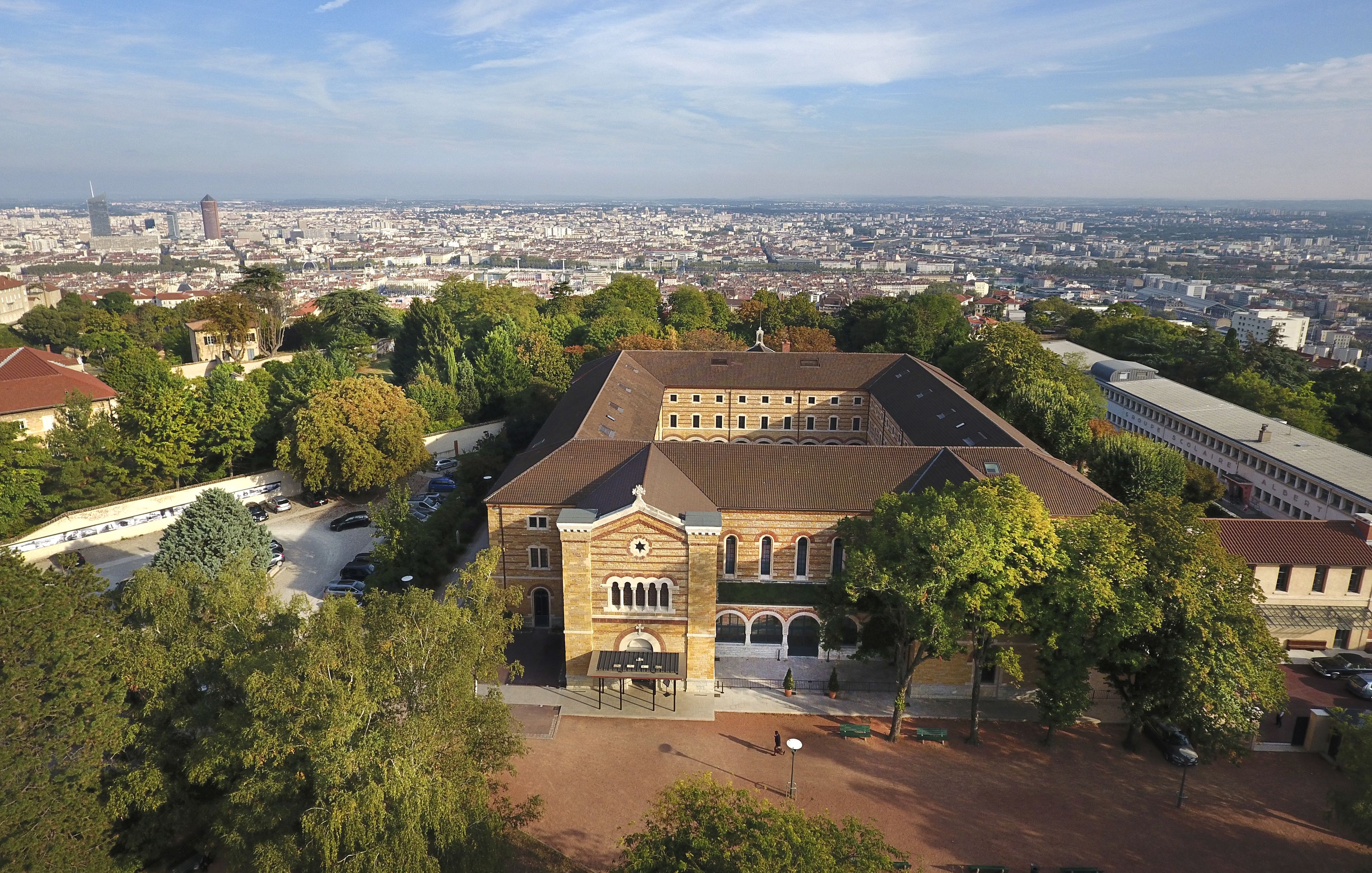 A large building with a central courtyard, surrounded by trees and a parking area.