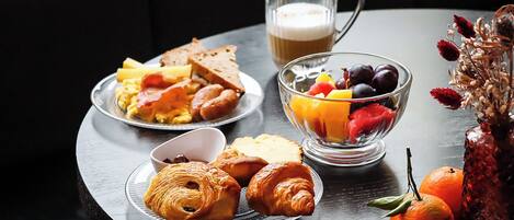 A breakfast setting with croissants, toast, eggs, and a fruit bowl on a table.