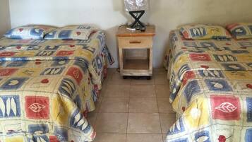 A room with two beds, each with a colorful quilt. There is a small wooden nightstand with a lamp between the beds.