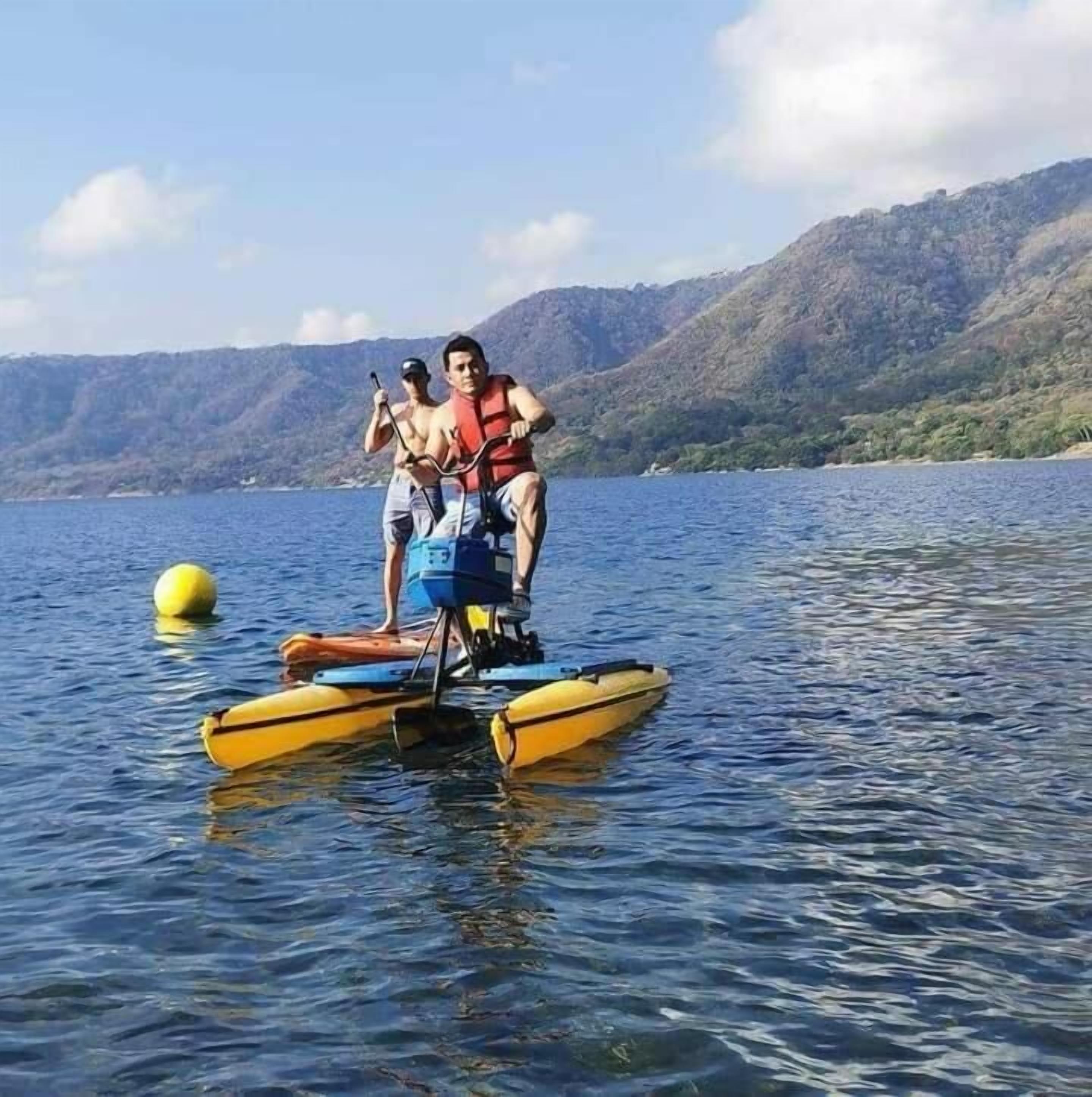 Due persone su una barca gialla gonfiabile in un lago, con delle colline sullo sfondo.