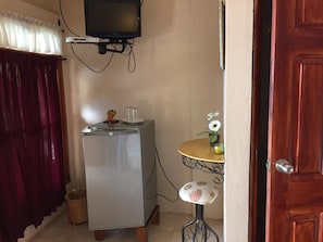 A compact room with a refrigerator, a small table with a vase of flowers, a television mounted on the wall, and a wooden door. - Posada Ecologica La Abuela (Catarina)