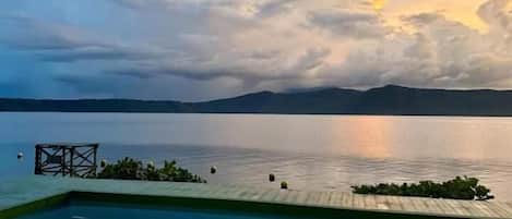 A swimming pool with a view of a calm lake and distant mountains.