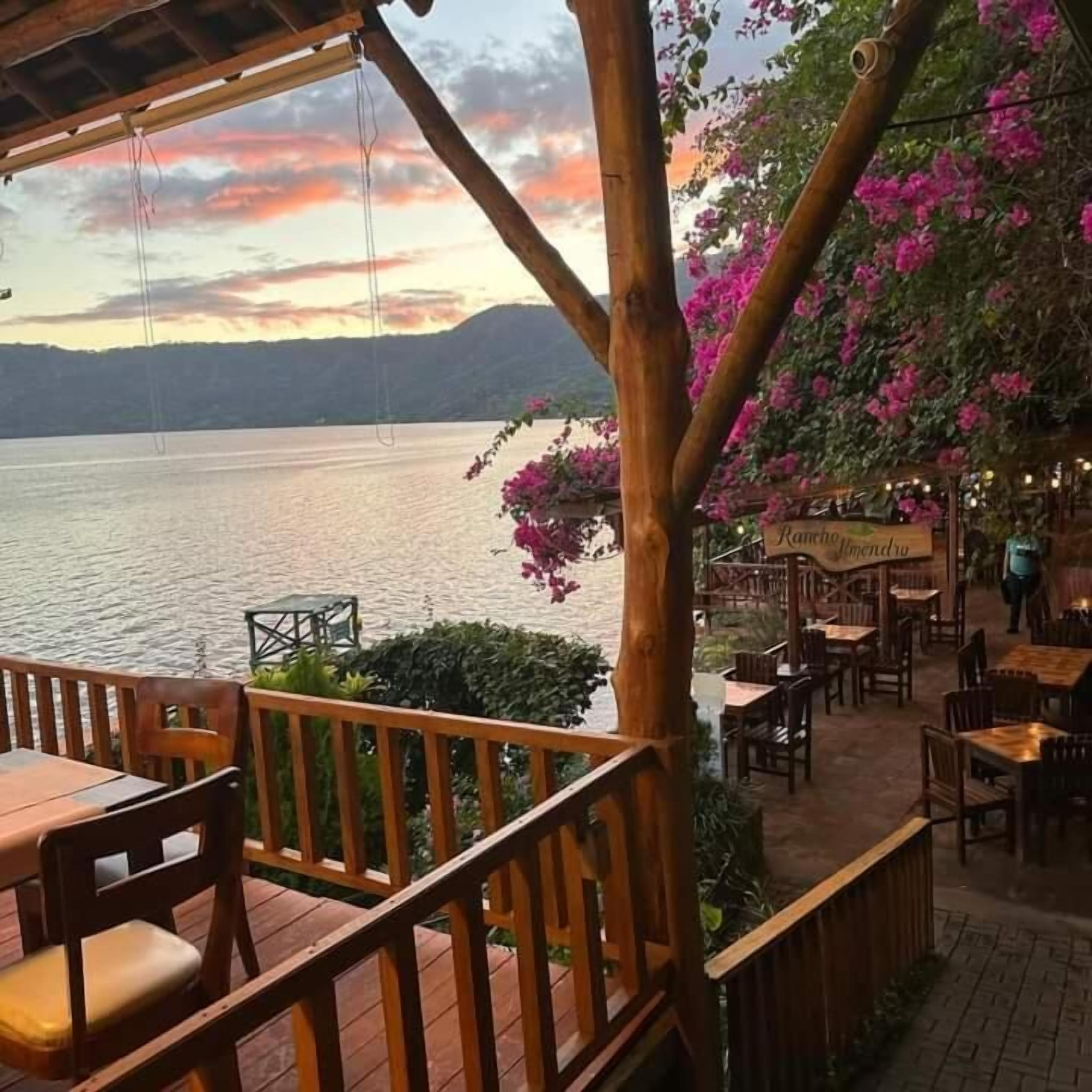 Un espace extérieur aménagé avec des tables et des chaises, offrant une vue sur une étendue d’eau et un paysage montagneux.