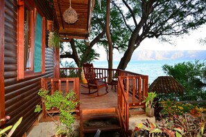 Une cabane en bois dotée d’une terrasse, de fauteuils à bascule et de plantes en pot.