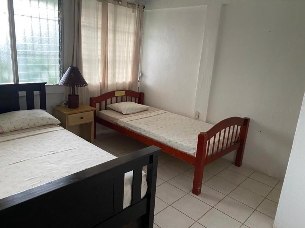 A single-bed room with a wooden headboard, a bedside table with a lamp, and a window with curtains.