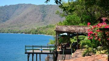 A wooden pier extending into a body of water, with a covered seating area and lush greenery.