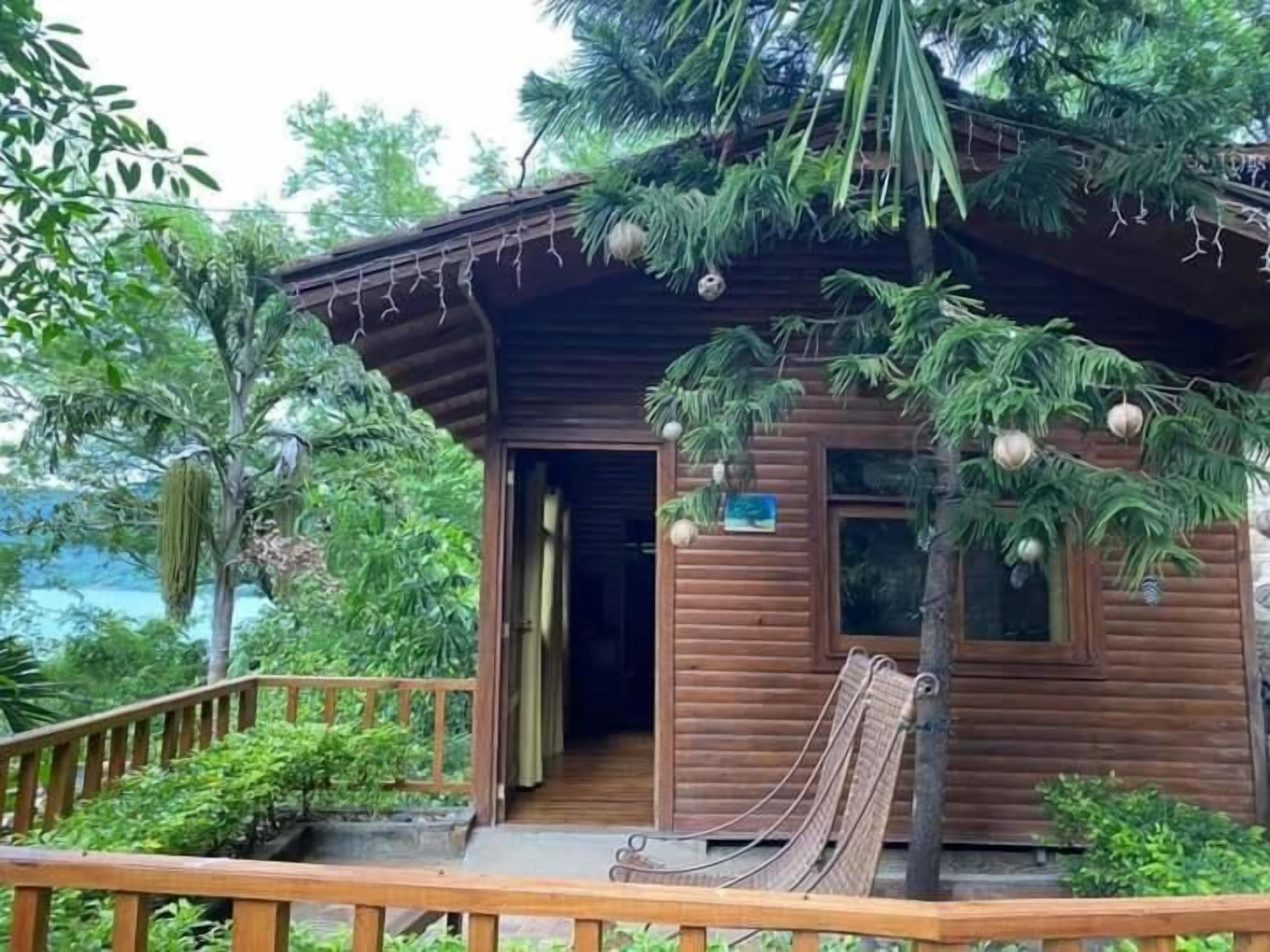 Uma cabana de madeira com varanda, rede e vista para o verde ao redor.