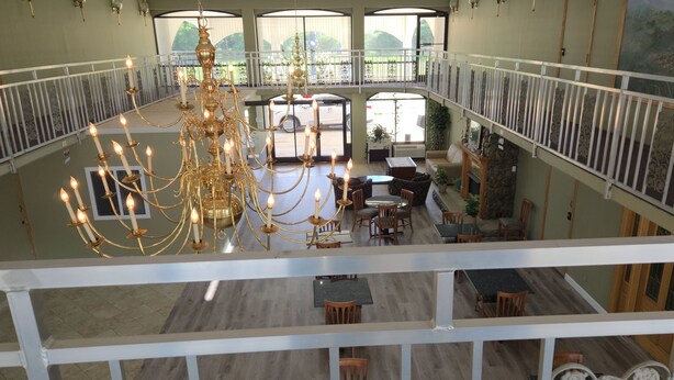 A multi-level hotel lobby with a grand chandelier, seating areas, and a view of the outdoors. - Americana Inn (Henderson)