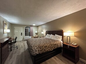 A hotel room with a large bed, a desk, a chair, and a telephone.