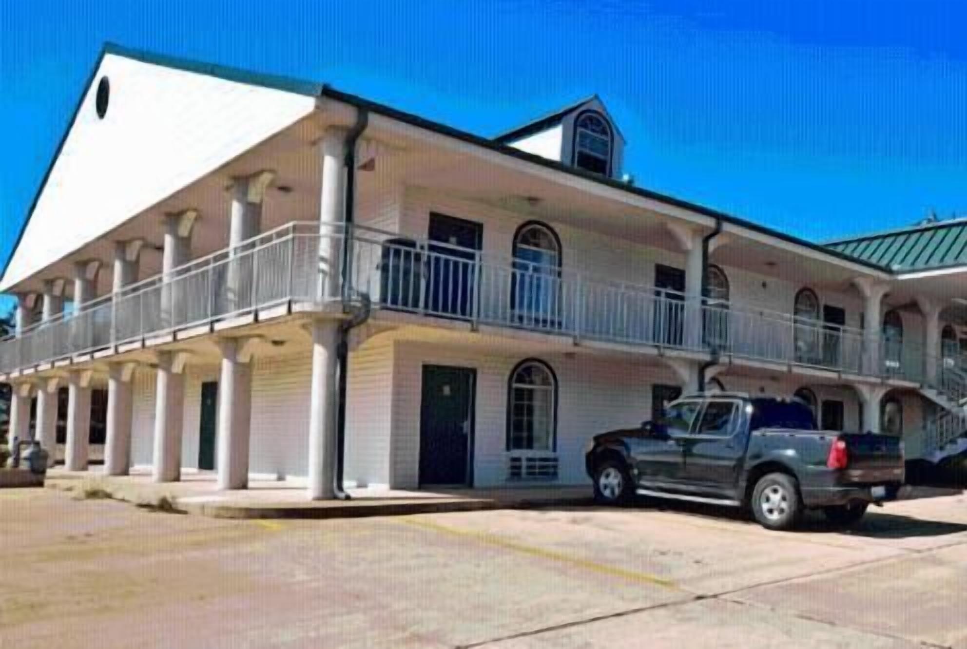 A two-story building with a balcony on the ground floor and a car parked in front.