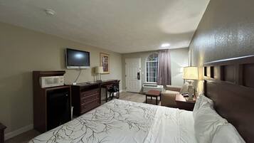 Habitación de hotel con cama, escritorio, televisor, silla y ventana con cortinas.
