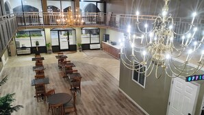 A spacious indoor area with multiple dining tables and chairs, a large chandelier, and a balcony with railings. - Americana Inn (Henderson)