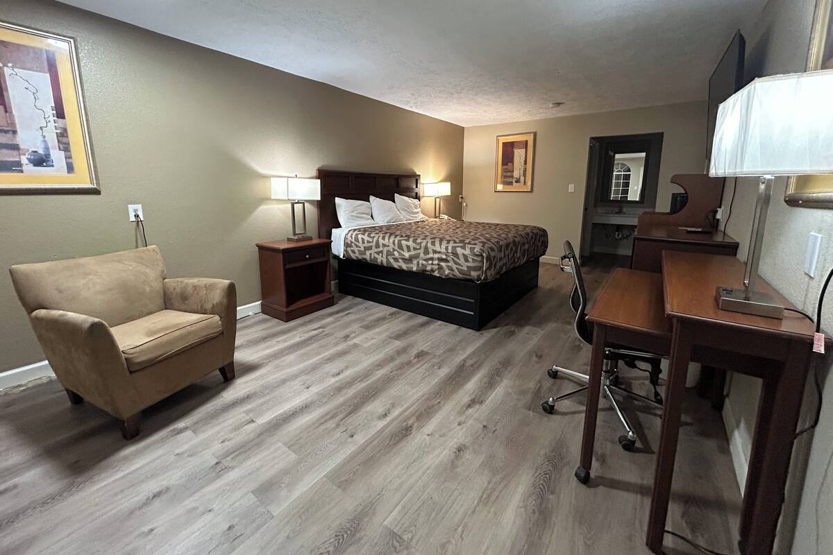 A hotel room with a bed, a desk, a chair, and a nightstand.
