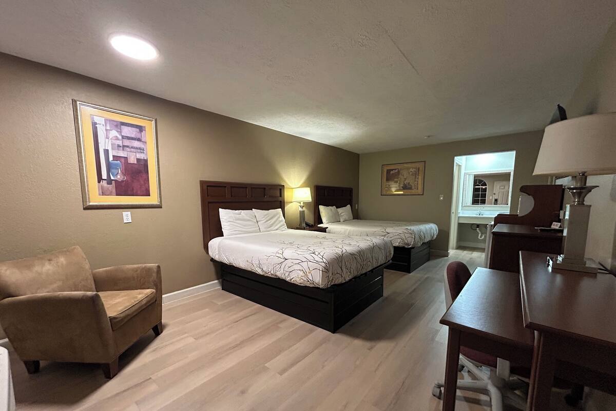 A hotel room with two beds, a desk, a chair, and a couch.