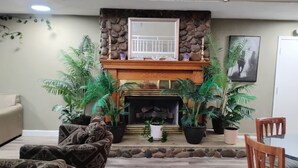 A living room with a fireplace, patterned sofas, and potted plants. - Americana Inn (Henderson)