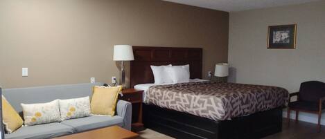 A hotel room with a bed, a sofa, a nightstand, a lamp, a chair, and a picture on the wall.