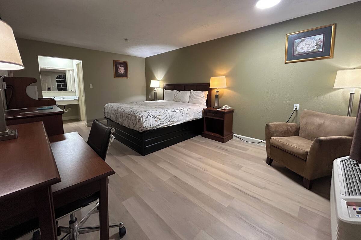 A hotel room with a bed, bedside tables, a desk, a chair, a lamp, a picture frame, and a mirror.