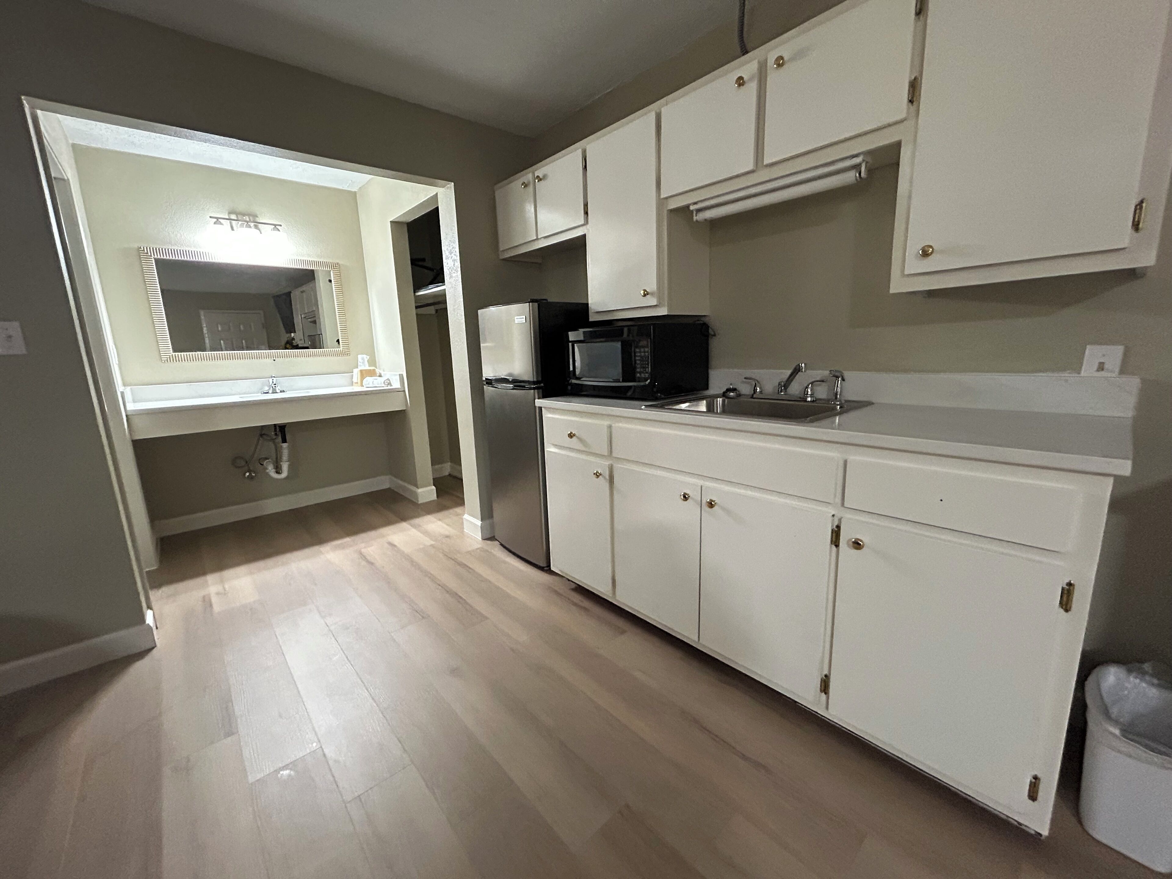 A kitchen with white cabinets, a stainless steel refrigerator, a microwave, and a sink.