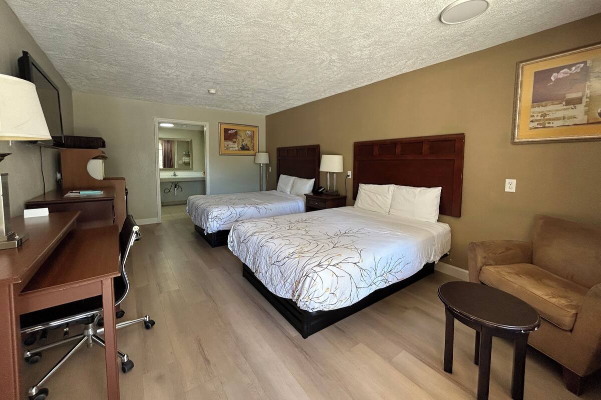 A hotel room with two beds, a desk, a chair, and a small table.