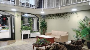 A spacious living area with a beige sofa, patterned armchairs, a coffee table, and a white desk. - Americana Inn (Henderson)