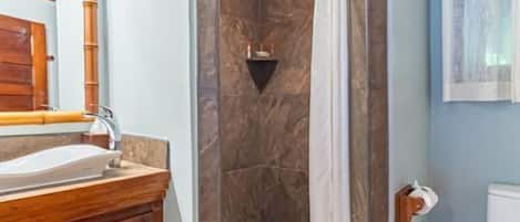 A bathroom with a wooden vanity, a shower with a marble wall, and a toilet.