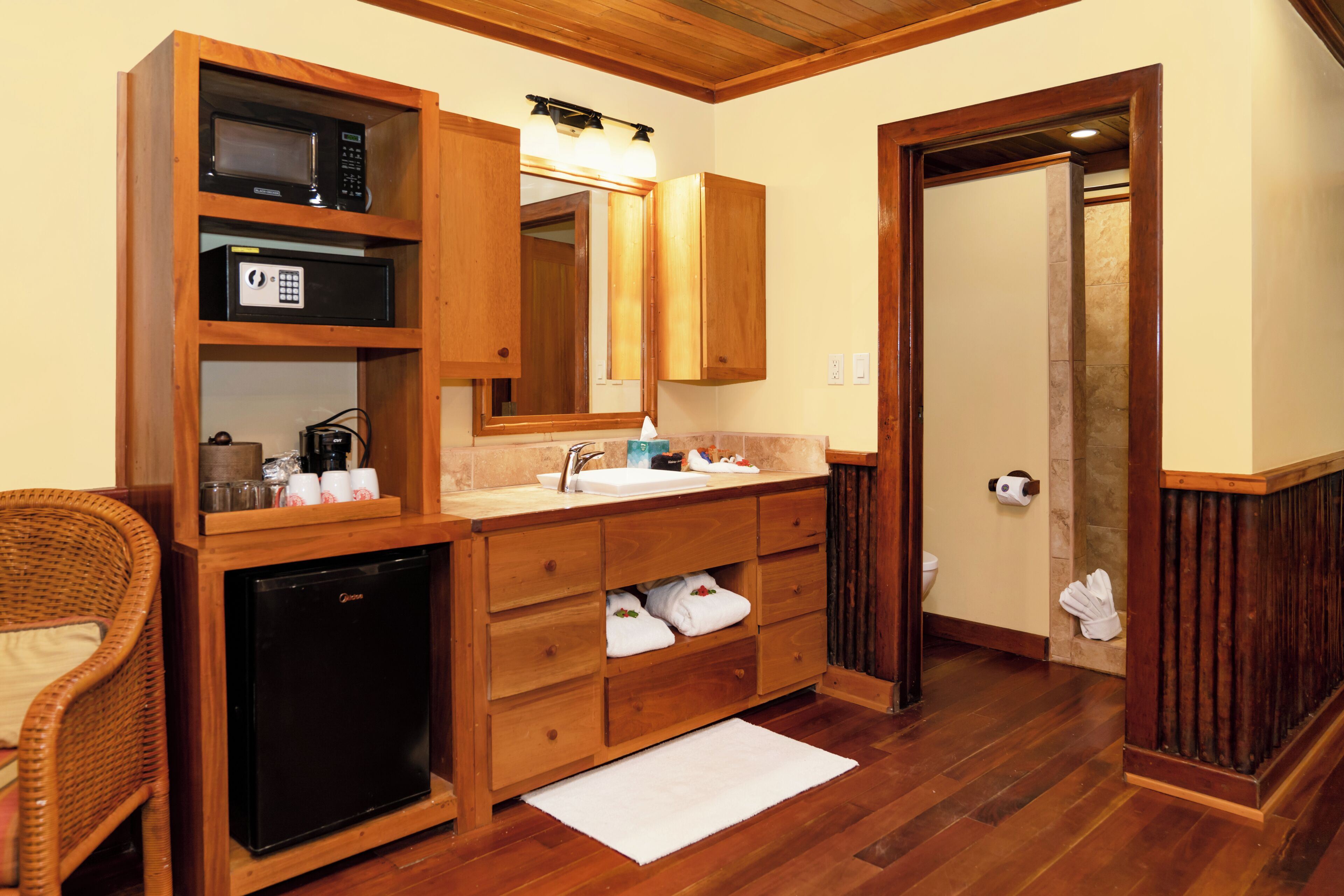 A bathroom with wooden cabinetry, a sink, a mirror, a microwave, and a small refrigerator.
