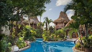 A pool area with thatched-roof structures and lush greenery. - Ramon's Village Resort (San Pedro)
