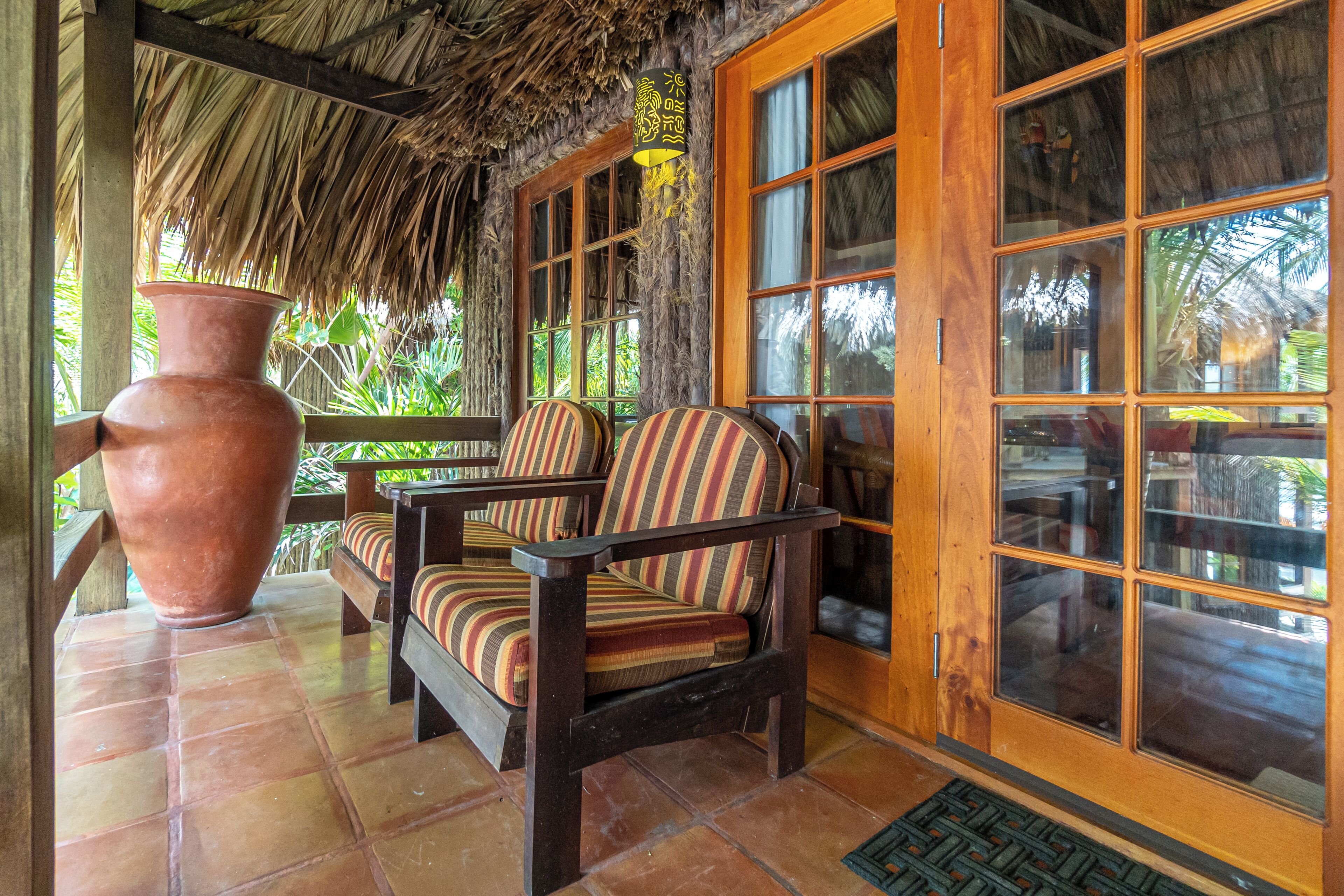 A covered porch with a thatched roof, wooden furniture, and large windows.