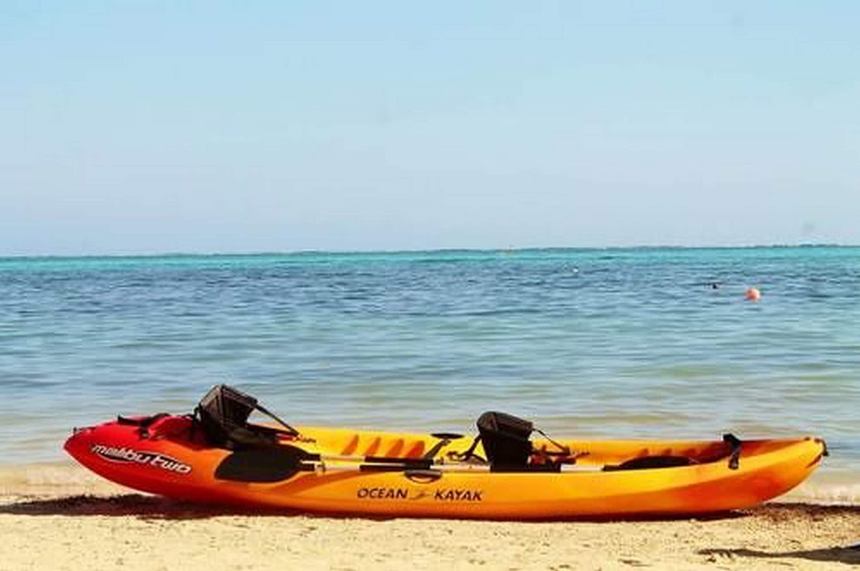 Een gele kajak met de tekst 'Ocean Kayak' erop, afgemeerd aan een zandstrand.