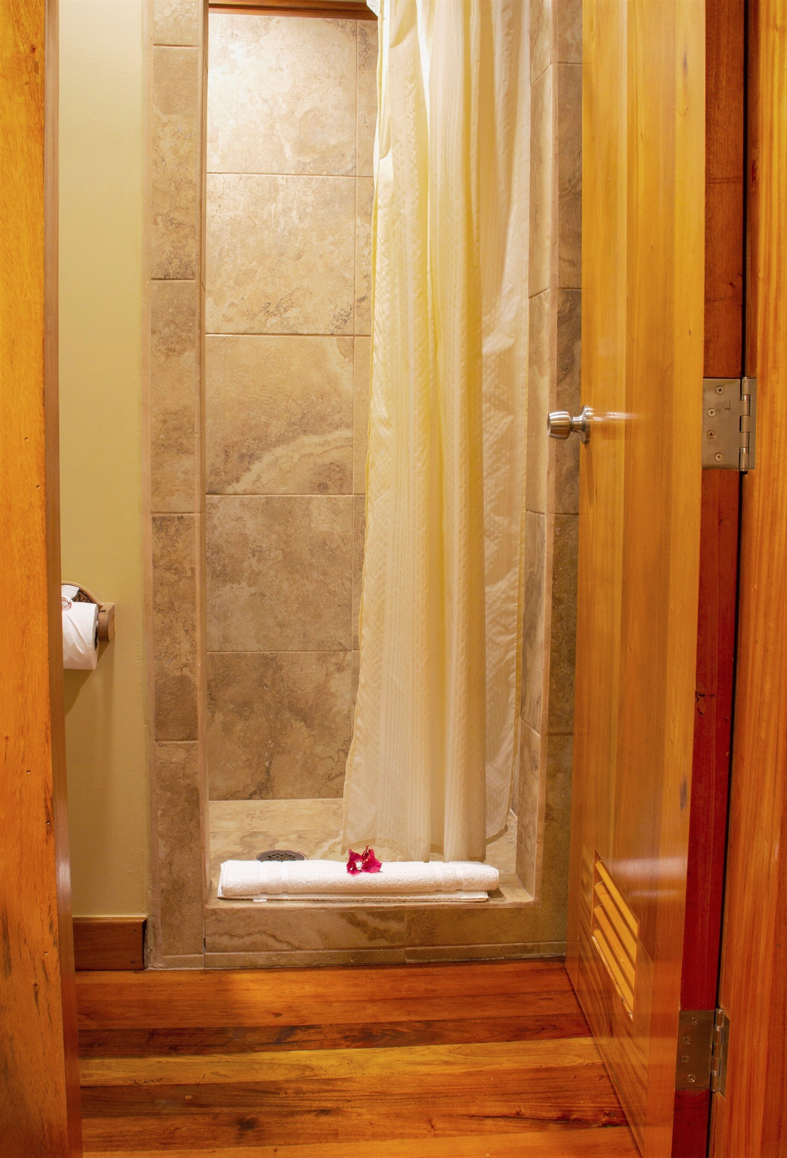 A bathroom with a shower, a towel rack, and a wooden floor.