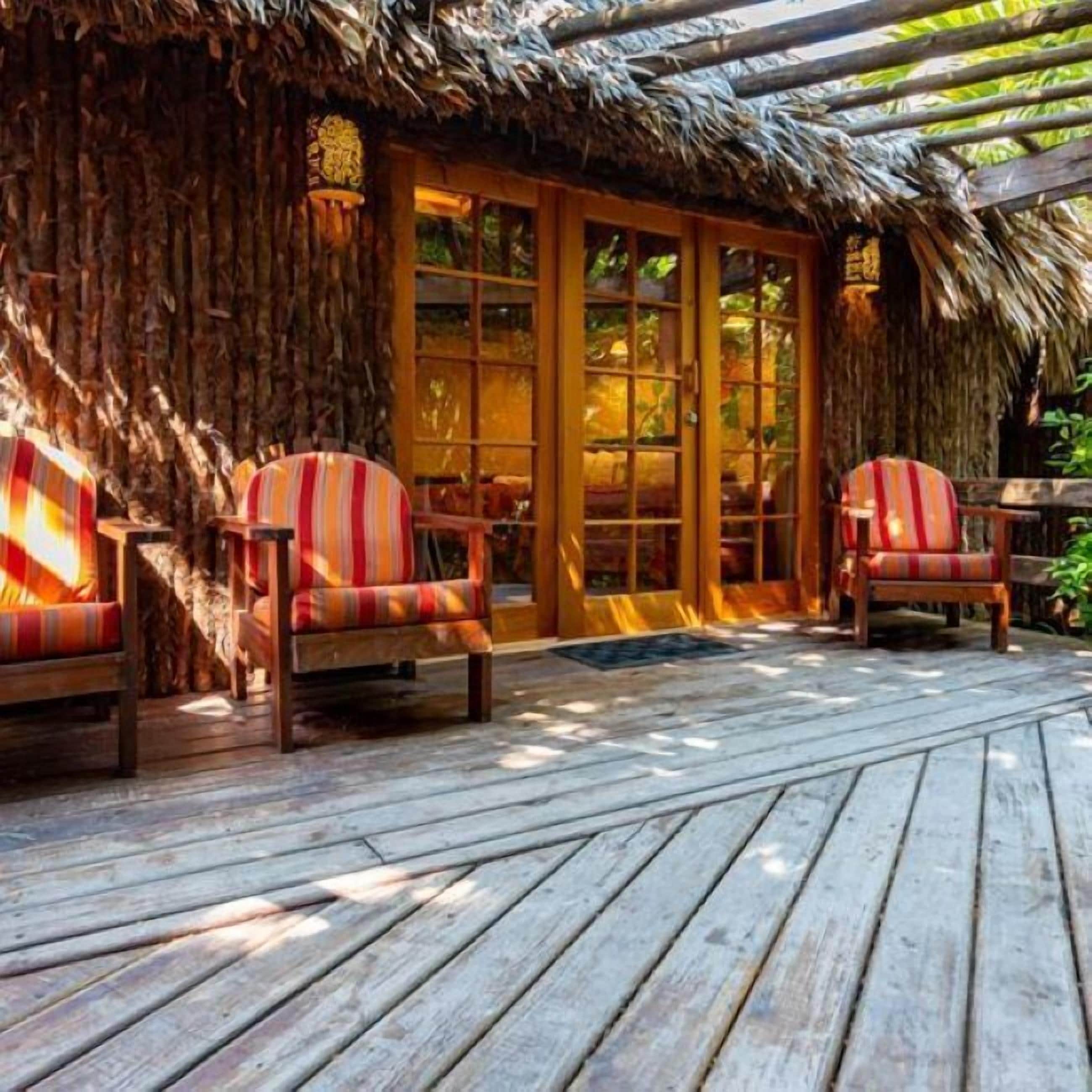 A wooden deck with two striped chairs and a thatched roof structure.
