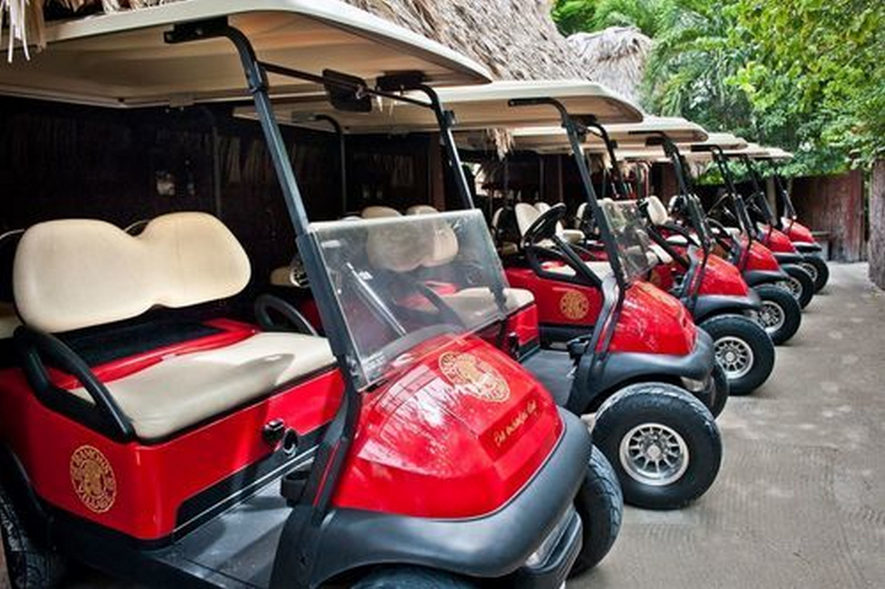 Une rangée de voiturettes de golf rouges, dotées de sièges beiges, est garée à l’extérieur.