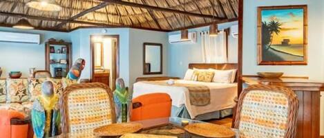 A room with a thatched roof, wicker furniture, and a painting of a beach scene.