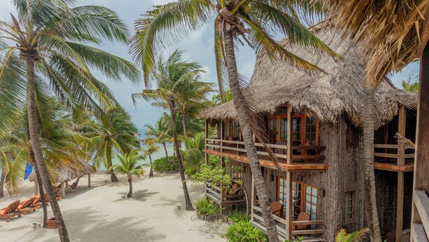A beach house with a thatched roof, wooden balconies, and a sandy beach with palm trees. - Ramon's Village Resort (San Pedro)