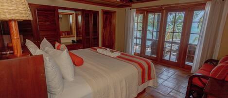 A spacious bedroom with a large bed, wooden furniture, and a view of the beach through large windows.