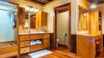 Un baño con armarios de madera, tocador, espejo y zona de ducha.