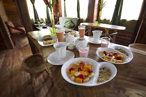 Una colazione con diversi piatti, tra cui frutta, cereali e bevande, disposti su un tavolo di legno in una stanza accogliente e rustica, con pareti in mattoni e una finestra.