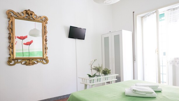 A hotel room with a green bedspread, a framed picture of red flowers, a television, a white wardrobe, and a small table with a plant. - Next Stop Roma Affittacamere Casilino (Rome)