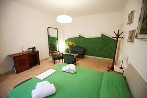 A hotel room with a green bedspread, a wooden desk, a chair, a mirror, a coat rack, and a lamp. - Next Stop Roma Affittacamere Casilino (Rome)