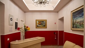 A reception area with a red and white color scheme, a reception desk, a vase with flowers, a painting, and a fire extinguisher. - Domus Napoleone (Rome)